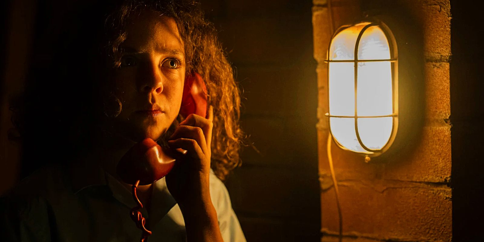 Eli Bell talks on a red phone next to a light in Boy Swallows Universe.