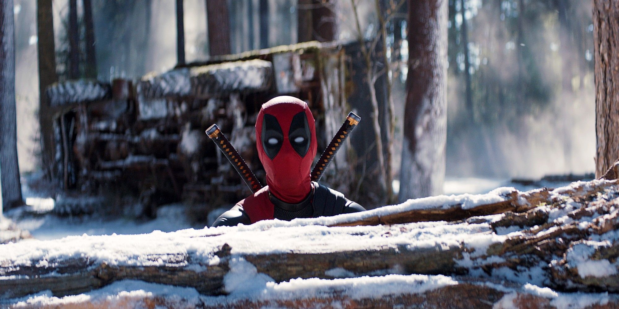 Ryan Reynolds como Deadpool fantasiado, enfiando a cabeça para cima, passando por um tronco caído na neve em Deadpool e Wolverine